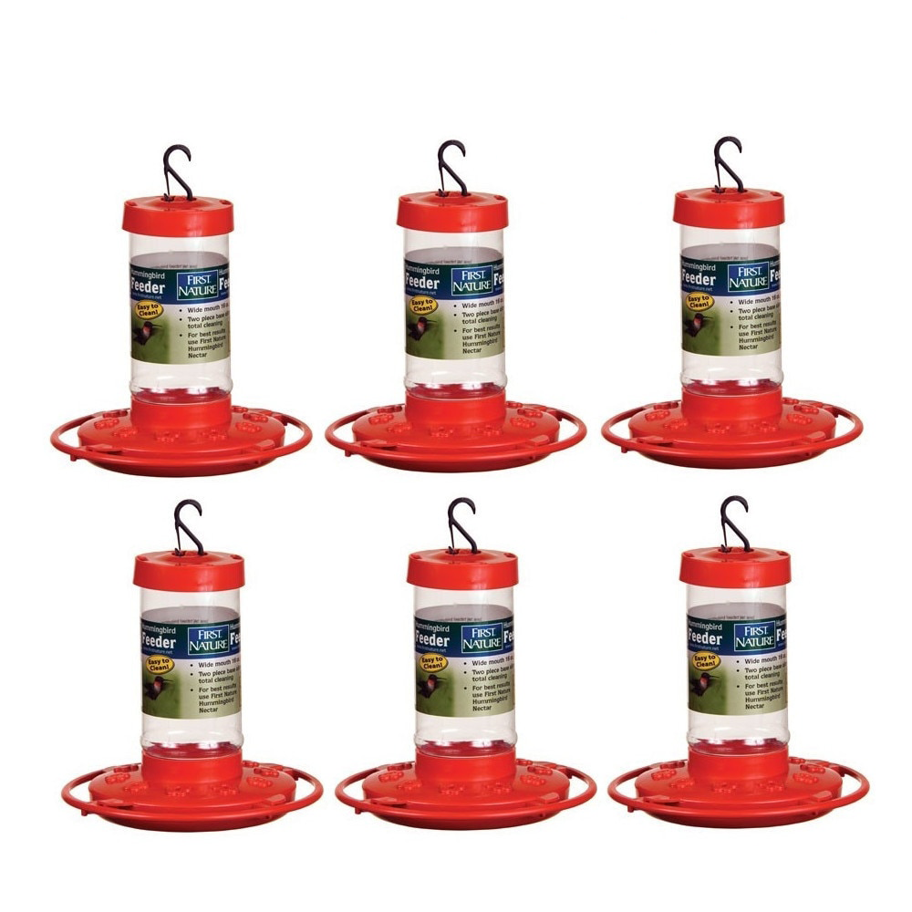 Product shot showing six First Nature hummingbird feeders with red bases and clear reservoirs against a white background