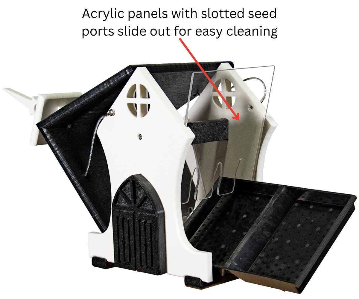 Product shot showing a white and black birdhouse style bird feeder with removable acrylic seed panels and a pull-out tray featuring a small arched door and cross-shaped window details