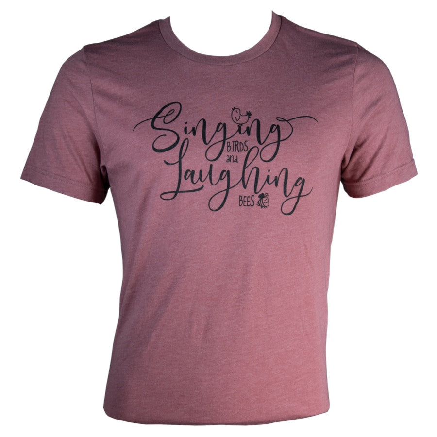 Dusty rose t-shirt featuring a black design that says Singing Birds and Laughing Bees with small illustrative bird and bee icons in a stylish script font