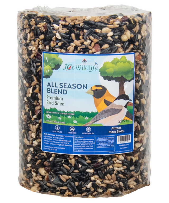 JCs Wildlife All Season Blend Premium Bird Seed shows a blend of black oil sunflower seeds, shelled peanuts, and cranberries in a clear plastic cylinder package with images of cardinals and chickadees on the label.