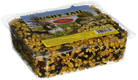 Pine Tree Farms Bushy Tail Superior Blend Squirrel Cake in a clear plastic container showing yellow corn black sunflower seeds and other nuts for year round feeding