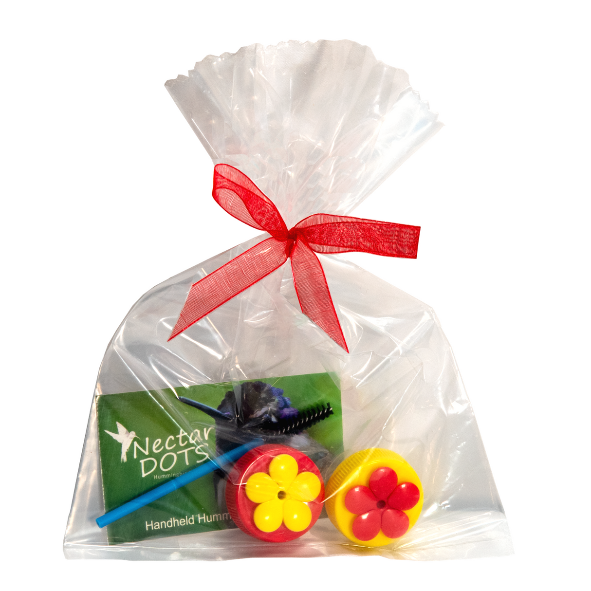 Product photography showing a clear cellophane bag tied with a red ribbon containing Nectar Dots hummingbird feeders two red and yellow flower-shaped caps a blue cleaning brush and a green instruction card