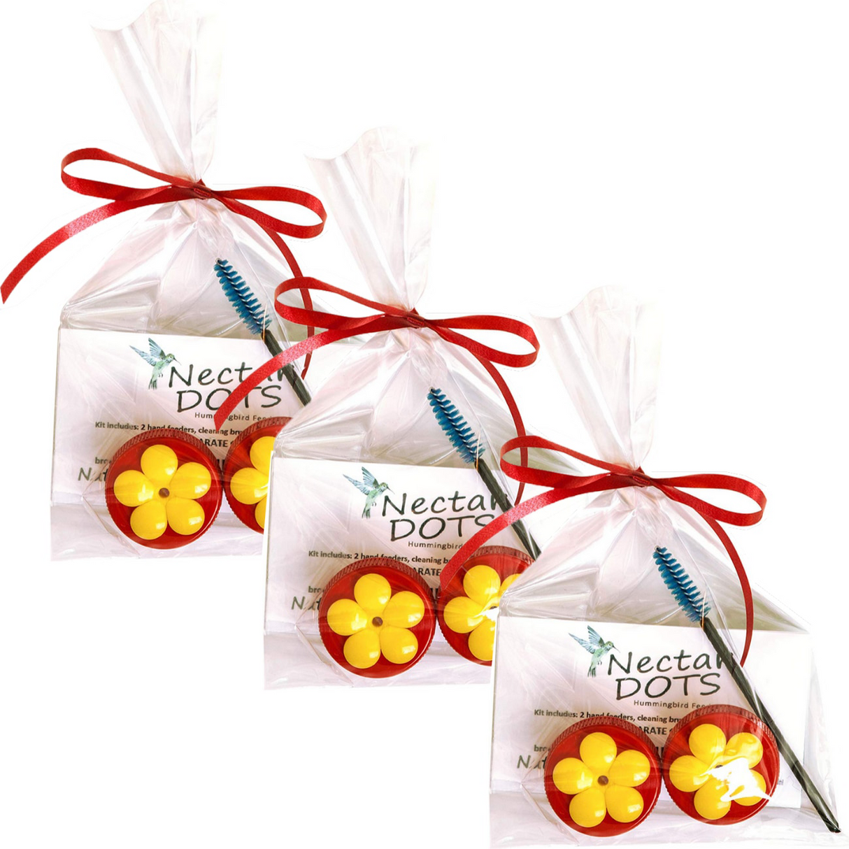 Product photography showing three Nectar Dots hummingbird feeder kits each containing two red and yellow flower-shaped feeders a cleaning brush and a red ribbon