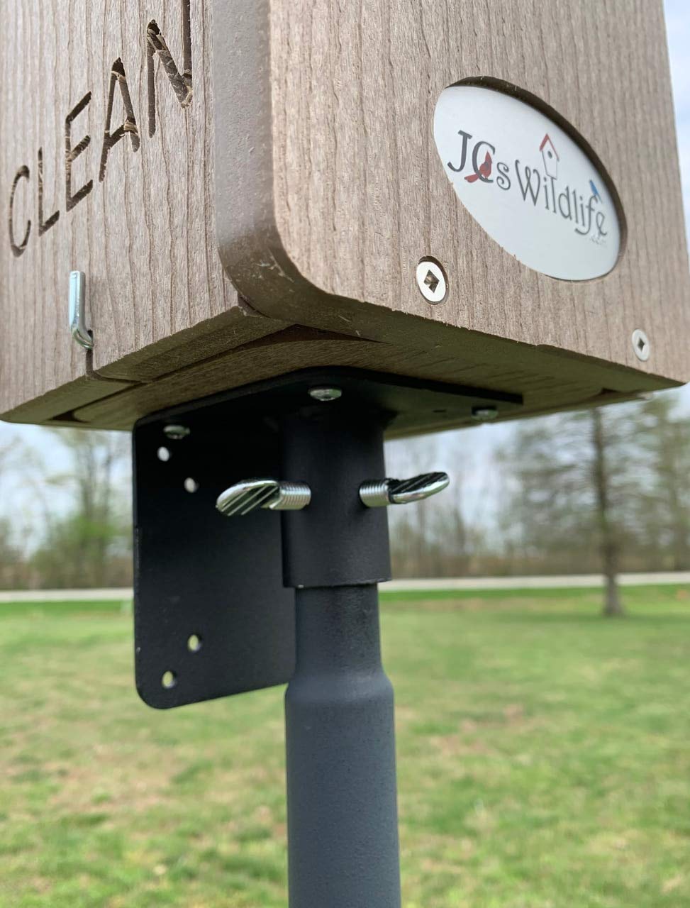 JQs Wildlife wood bird feeder with Clean sign on a black metal post outdoors featuring wing nut fasteners and a logo with birdhouse graphic