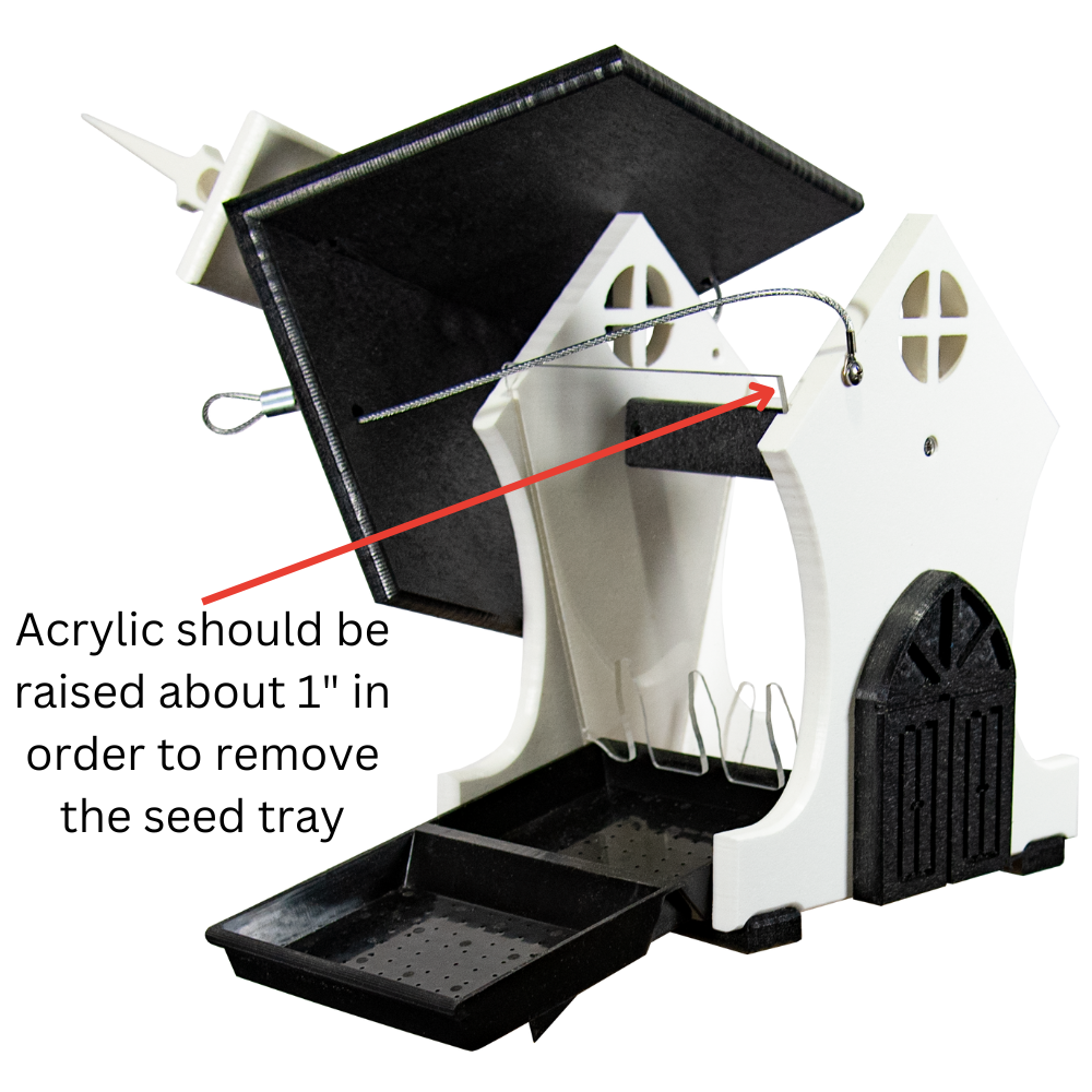Product shot of a white and black acrylic bird feeder shaped like a house with a pull-out seed tray and a detailed, gothic-style base featuring small windows and a peaked roof.