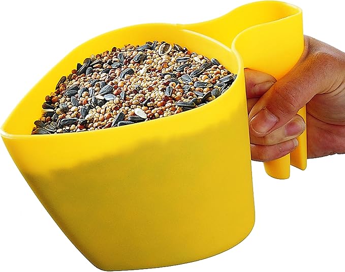 Plastic scoop filled with a mix of birdseed including sunflower seeds millet and niger seeds held in a hand showing its bright yellow color and ergonomic handle
