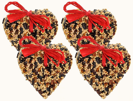 Four handmade birdseed hearts adorned with bright red raffia bows feature a mix of sunflower seeds millet and pecans against a white background