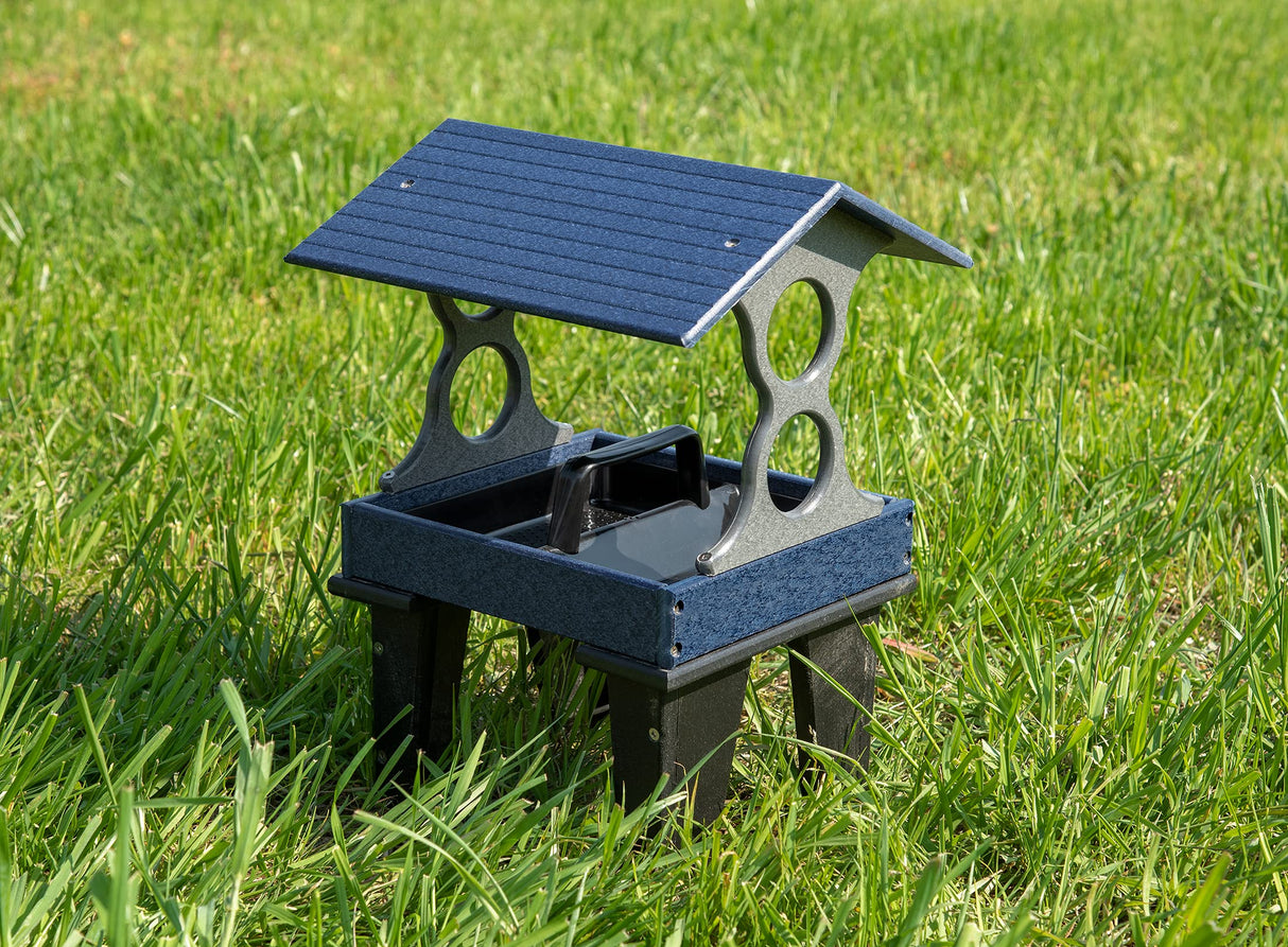 Plastic bird feeder on green grass featuring a dark blue peaked roof gray base and black legs