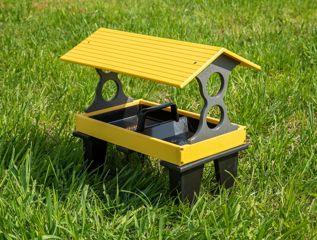 Plastic bird feeder in vibrant yellow and black on a lush green lawn with a protective roof and a convenient carrying handle