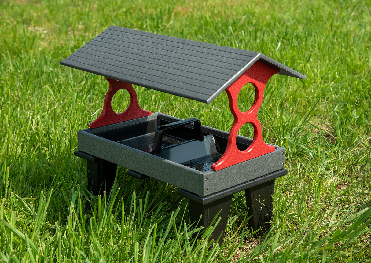 Plastic bird feeder on grass with a gray roof, red accents, and a black handle