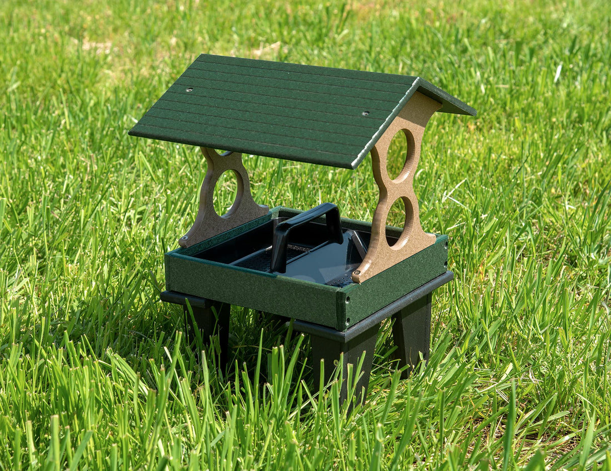 Plastic bird feeder on green grass with a dark green roof tan accents and a black tray