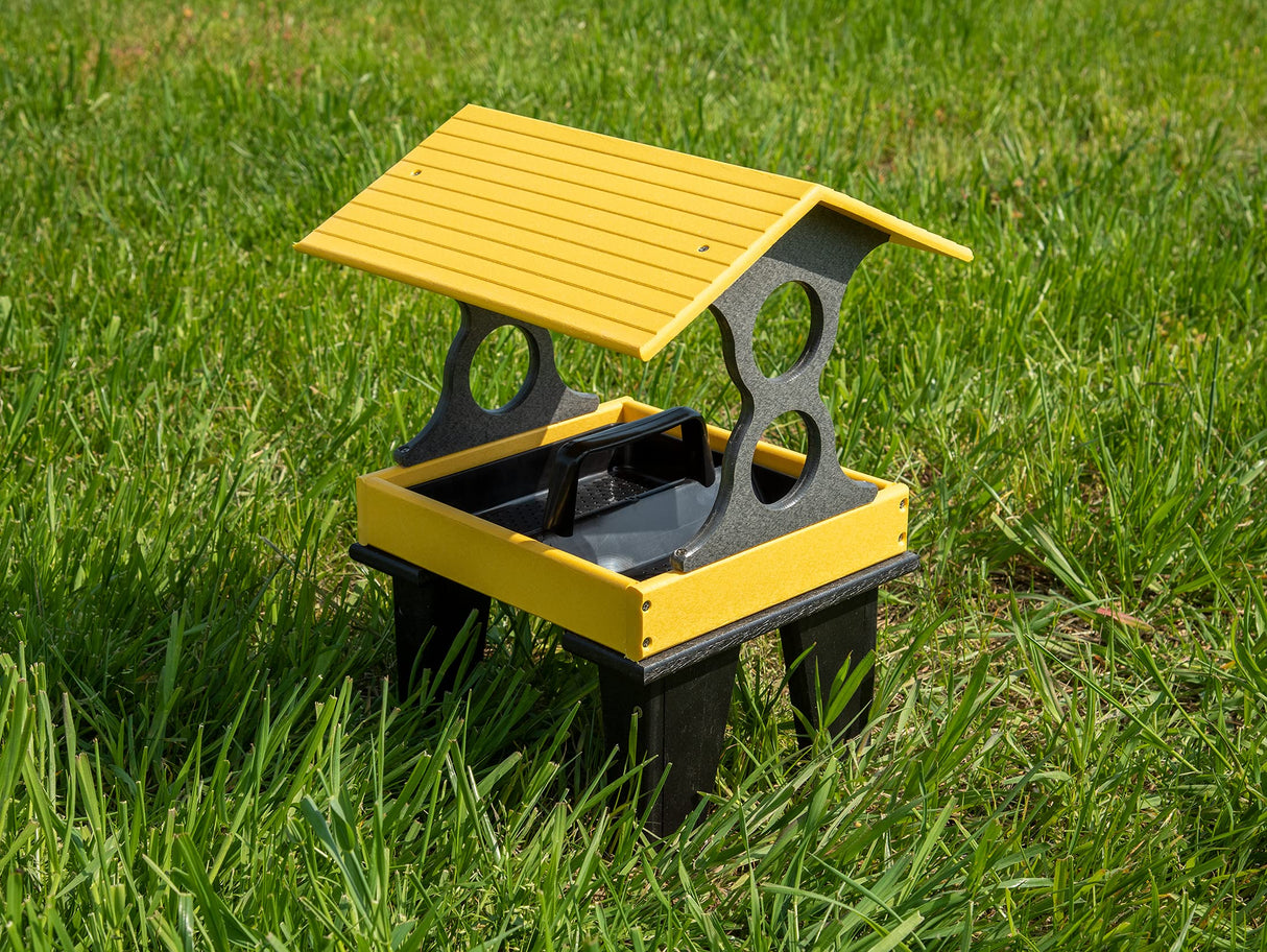 Plastic bird feeder on green grass featuring a yellow roof, black base and a convenient carrying handle