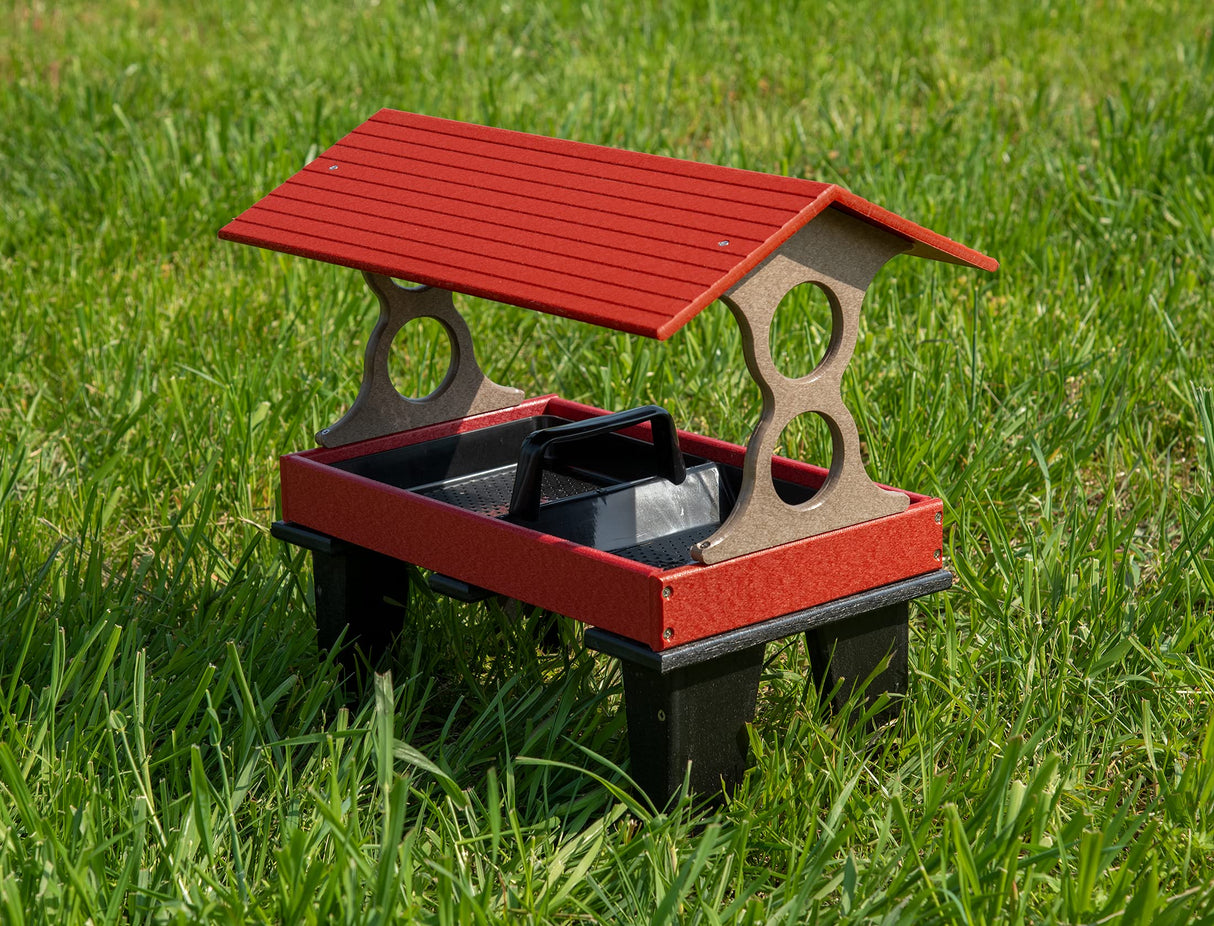 Recycled plastic bird feeder on green grass showing a red roof, black tray and taupe supports