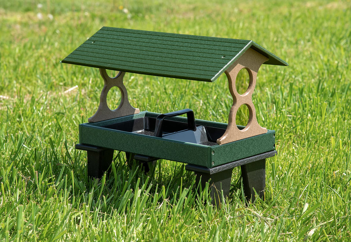 Plastic ground feeder with green roof and tan sides situated on a vibrant green lawn featuring a dark green tray and black legs