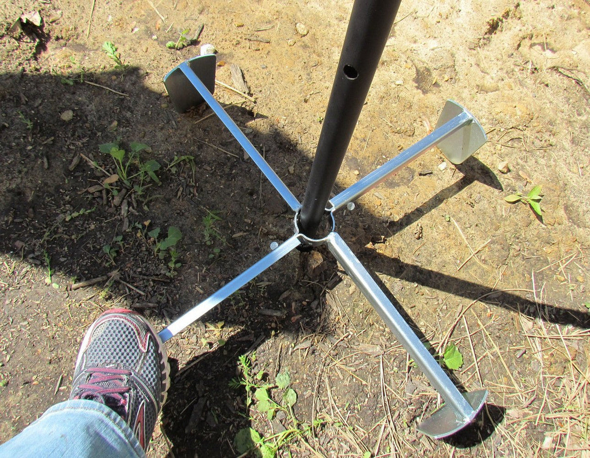 Photograph showing a metal ground stake with four stabilizing feet in the ground near small plants and dry twigs