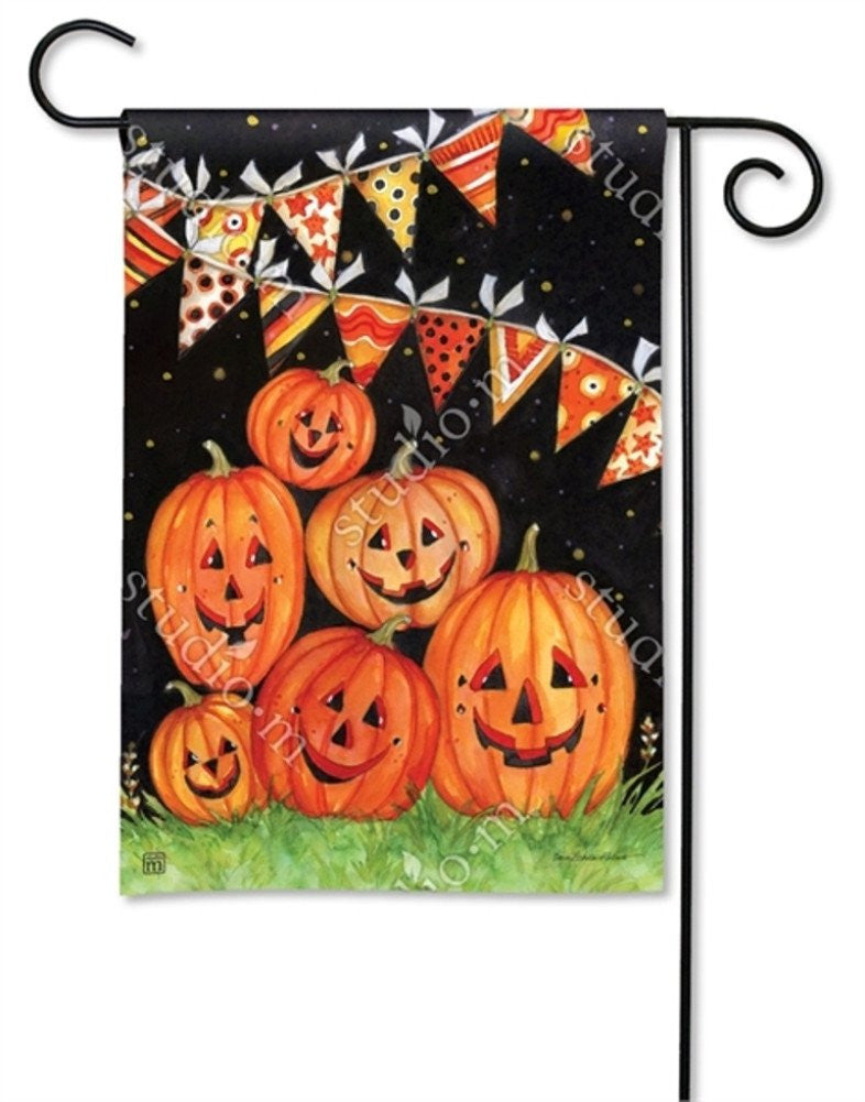 Susan Winget's watercolor garden flag depicts smiling jack-o'-lanterns in a grassy patch under a night sky adorned with colorful Halloween bunting and sparkling stars