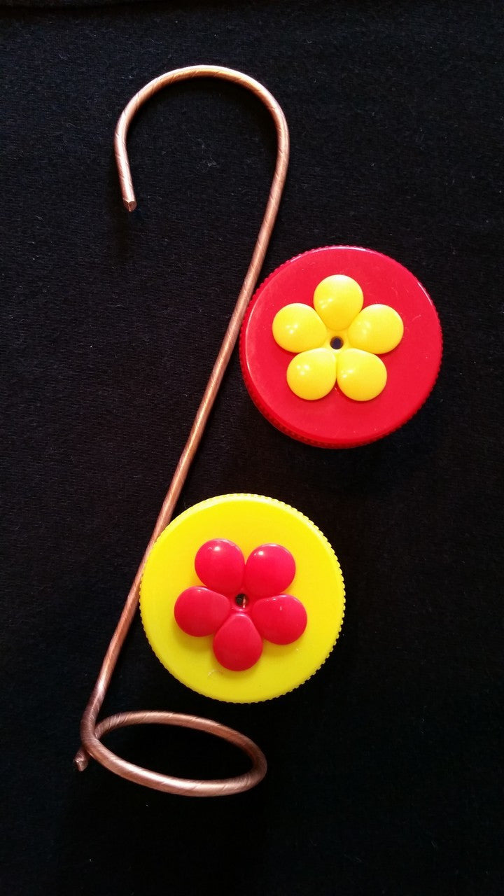 Copper wire hummingbird feeder with red and yellow flower-shaped bottle caps against a black background