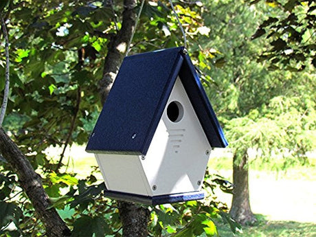 Recycled plastic birdhouse hanging from a tree in a garden featuring a navy blue roof white body and ventilation slots showcasing a charming rustic aesthetic