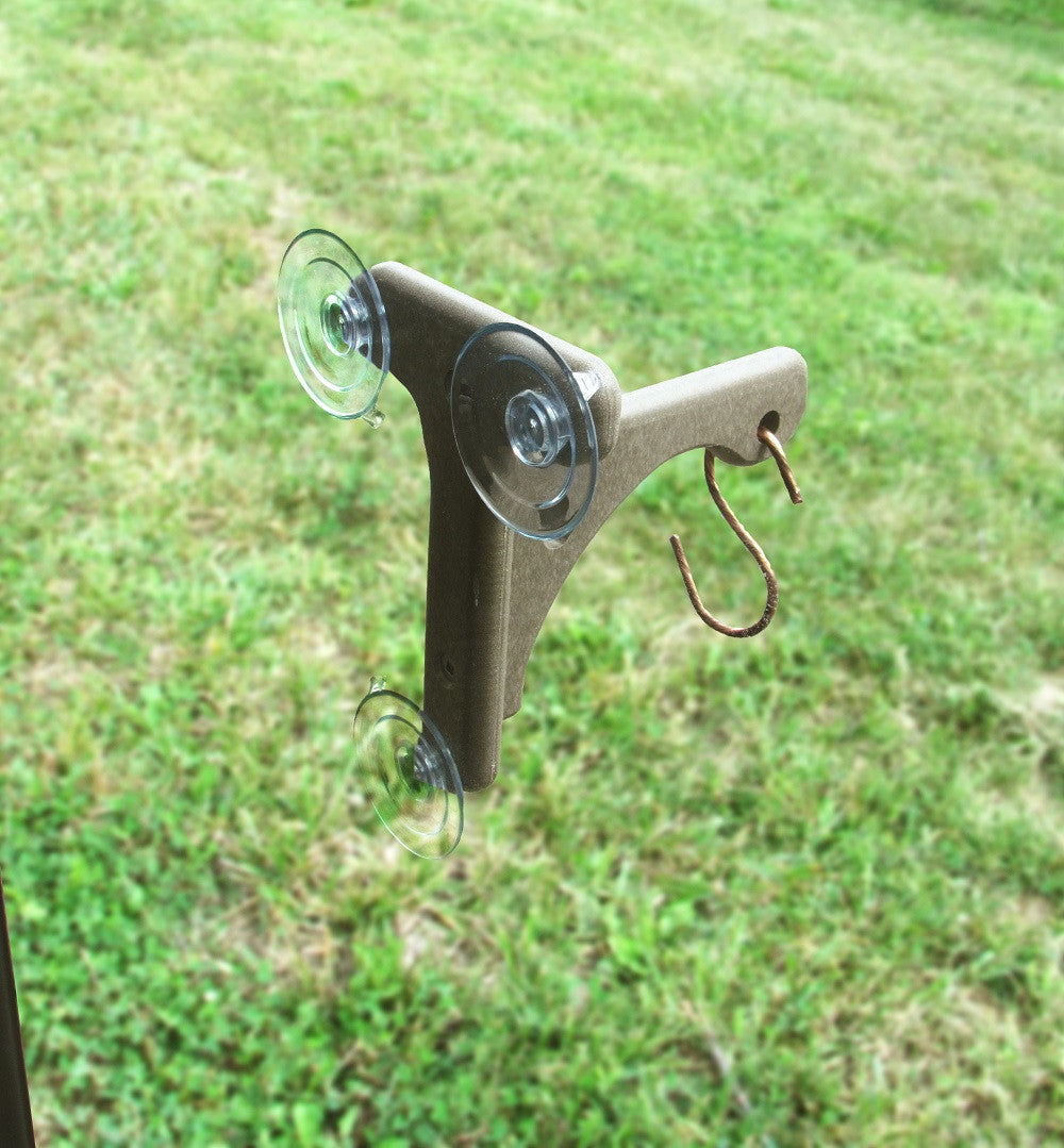 Unknown artist photograph of a brown plastic suction cup window feeder with three suction cups and a copper S-hook against a blurred green grass background