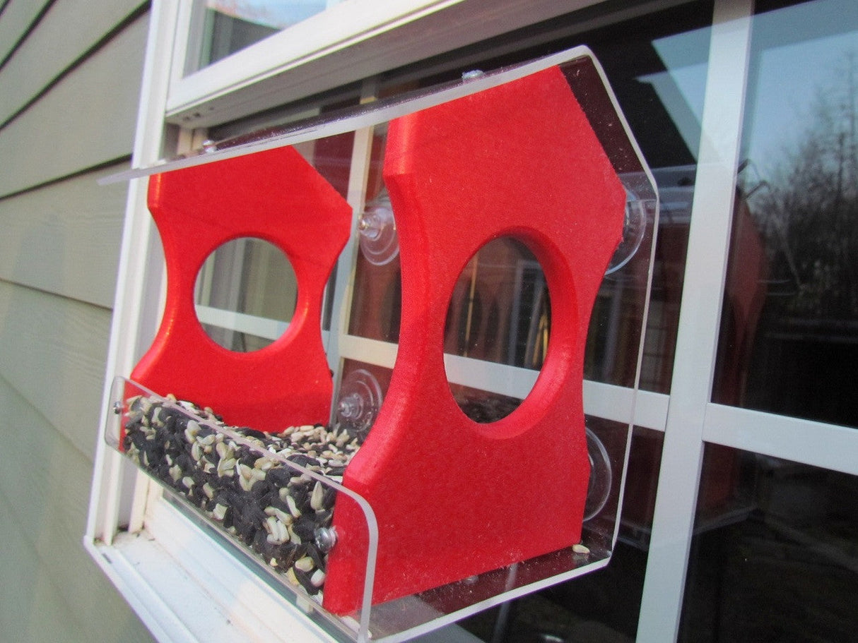 3D-printed red acrylic bird feeder on a window showcasing sunflower seeds vibrant red color and clear acrylic accents