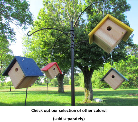 Handcrafted birdhouses with blue, red, yellow, and gray roofs hanging from a metal stand in a lush green yard near leafy trees