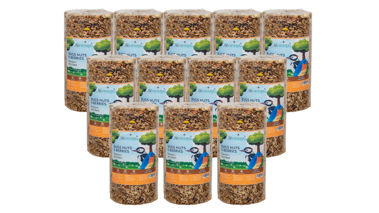 JCs Wildlife product photography showing twelve cylinders of Bugs Nuts & Berries premium bird seed featuring a woodpecker and bluebird against a green tree background with visible sunflower seeds nuts and berries