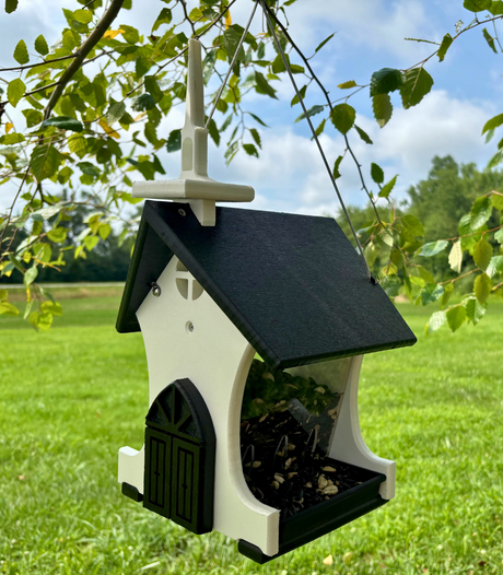 Plastic birdhouse feeder shaped like a church in a green field with a black roof and white steeple filled with birdseed