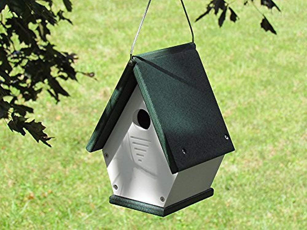 Recycled plastic birdhouse hanging outdoors features a dark green roof white body and ventilation slots against a lush green lawn background