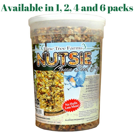 Pine Tree Farms Nutsie Classic Seed Log in a clear plastic container shows a mix of nuts, seeds, and dried fruit with a vibrant bluebird and the words No Hulls Less Mess