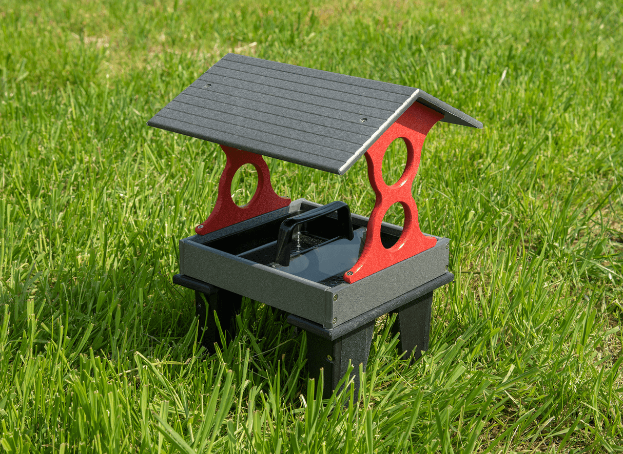 Plastic bird feeder on grass with a gray roof red supports and a black tray showing vibrant green grass