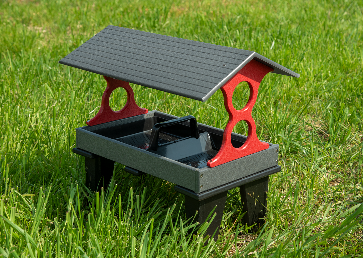 Plastic bird feeder on grass with gray roof red supports and black tray