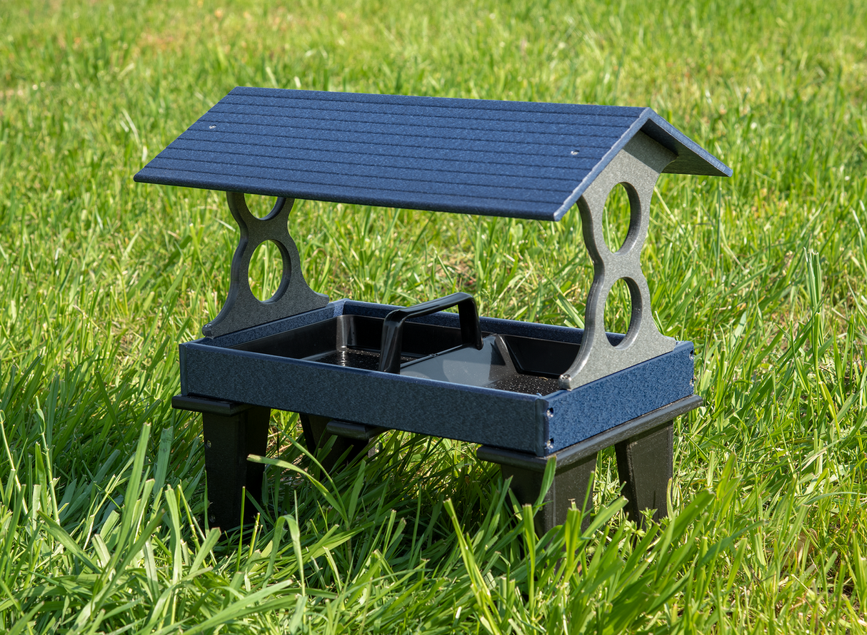 Plastic bird feeder on green grass featuring a dark blue speckled roof a gray speckled frame and a black central tray.