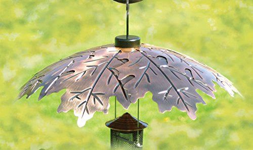 Metal leaf-design bird feeder hanging outdoors showing copper tones intricate details and a dark brown base against a blurred green background
