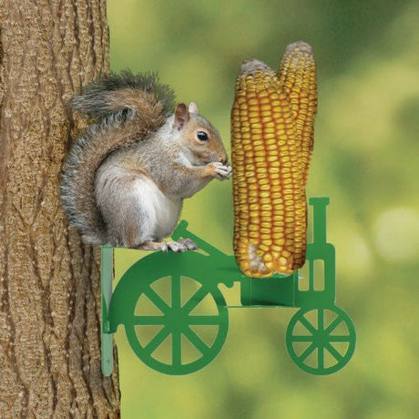Photograph of a gray squirrel on a tree eating corn from a green tractor-shaped feeder with bright yellow kernels and large spoked wheels