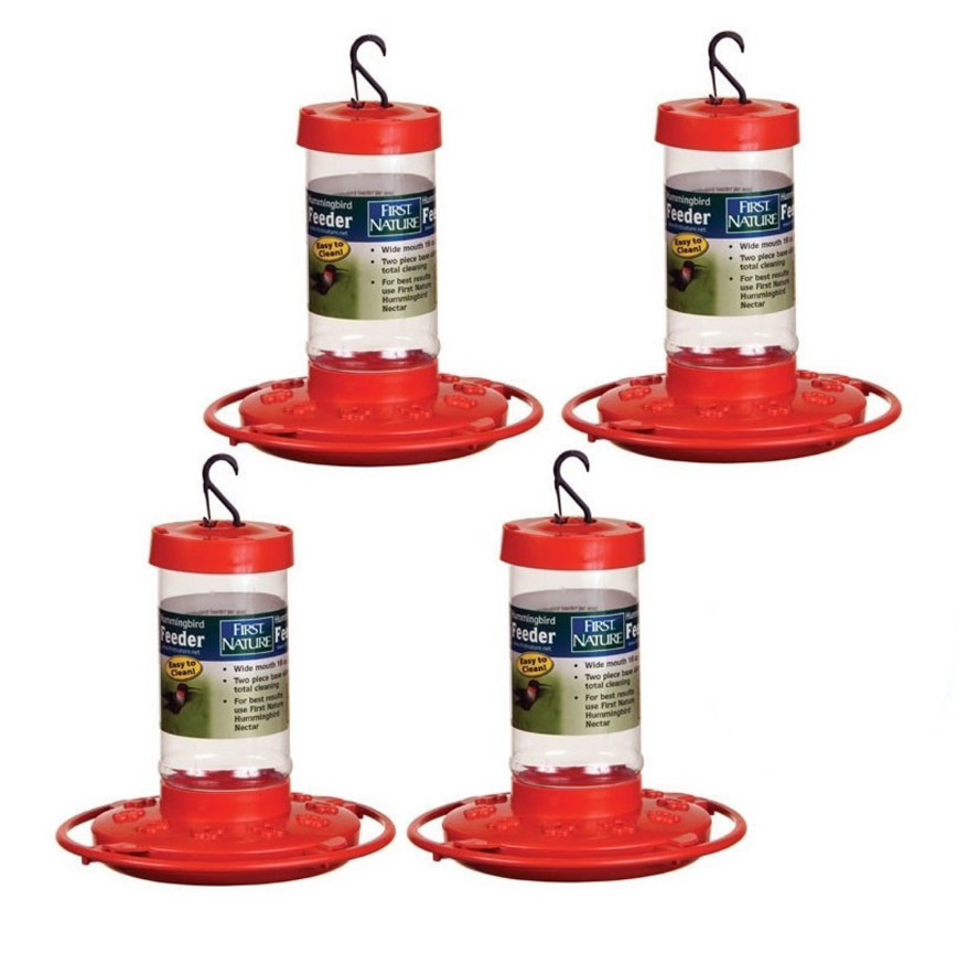 Product shot showing four First Nature hummingbird feeders with red bases clear reservoirs and hanging hooks against a white background