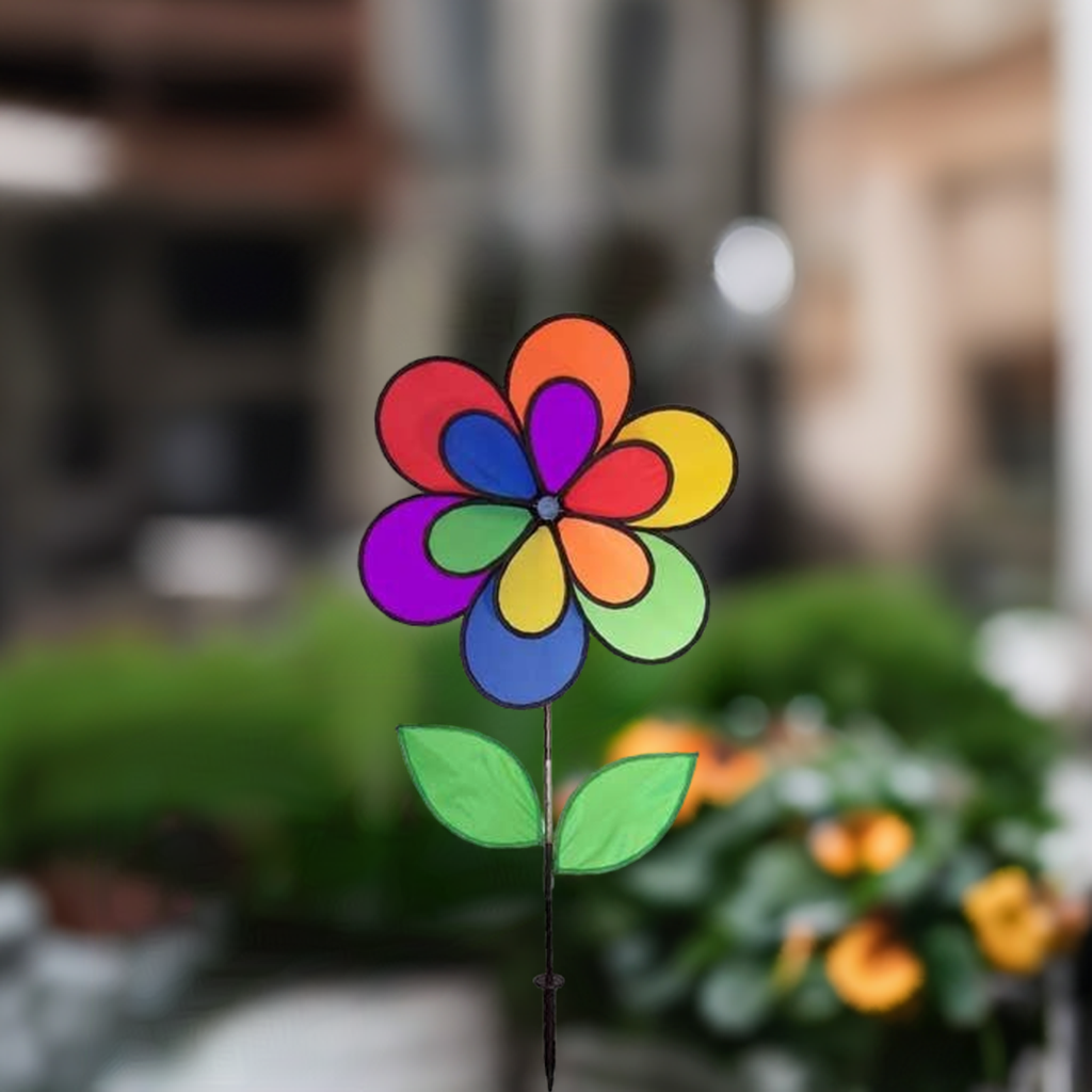 Rainbow wind spinner garden decoration with vibrant petals and green leaves in an outdoor setting with blurred background