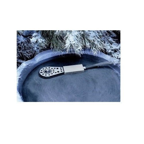 Photograph of a frost-protected outdoor water feature with a de-icer device featuring a perforated disc and a rectangular heating element surrounded by snow-dusted pine branches in a stone birdbath