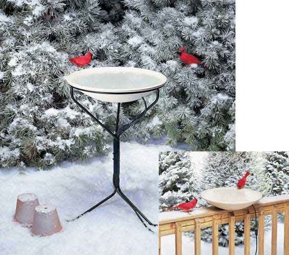 Heated bird bath with metal stand in snowy backyard, featuring red cardinals.