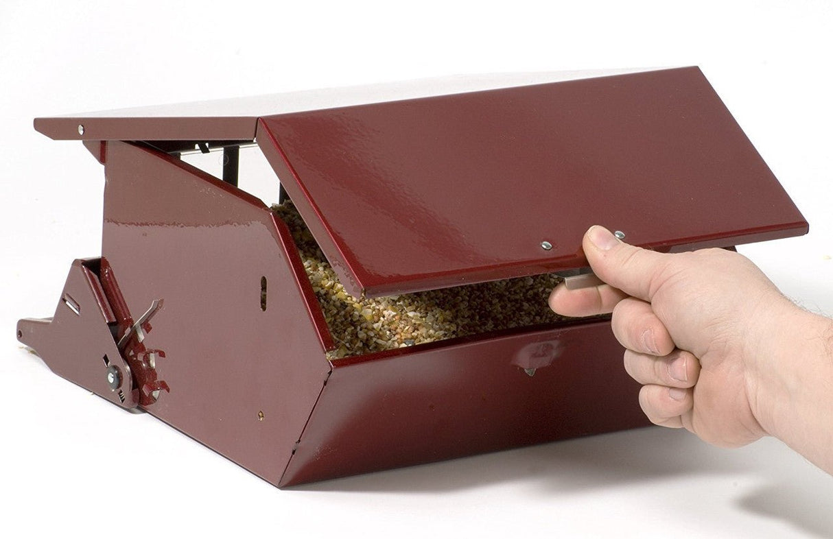 Red squirrel-proof bird feeder with adjustable weight settings being opened to refill with birdseed.