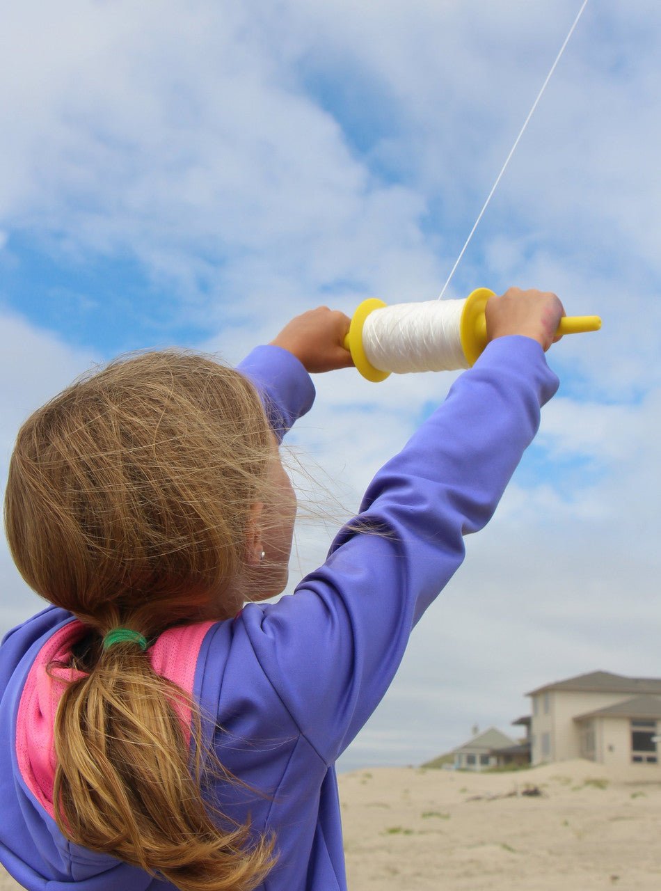 Child flying a kite with In The Breeze 50 LB x 500' Twisted Kite Line on a yellow spool on a sunny day at the beach.