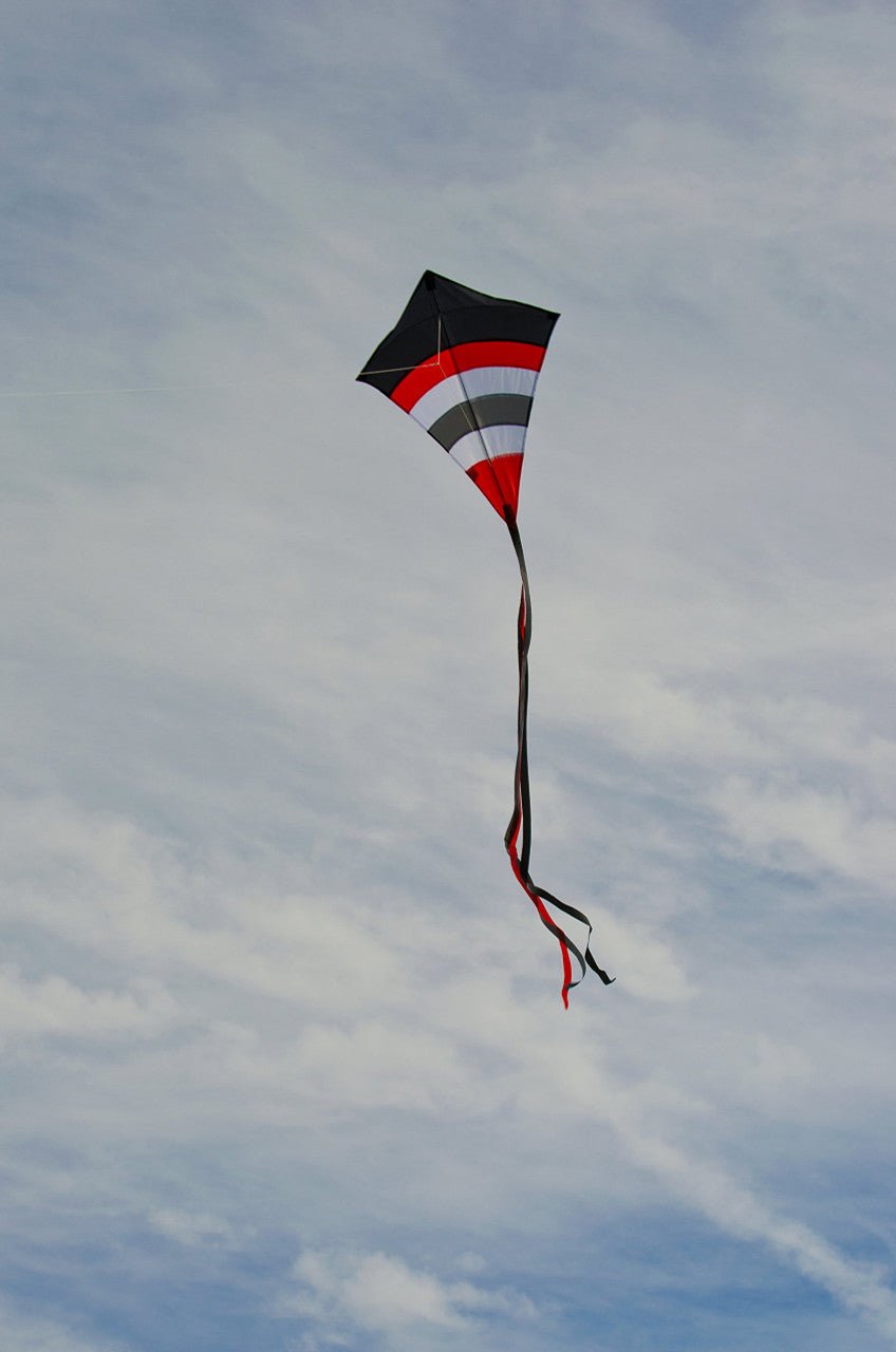 In the Breeze Blazer Arch 27" Diamond Kite flying in the sky with red, black, and white colors and long fabric tails.