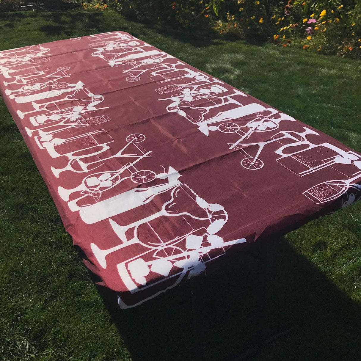 In the Breeze Happy Hour Drinks 6 Foot Fitted Tablecloth on a picnic table, featuring a fun drink-themed design.