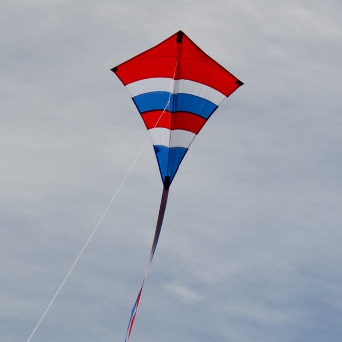 Patriotic Arch 27" Diamond Kite in red, white, and blue flying in the sky with long fabric tails.
