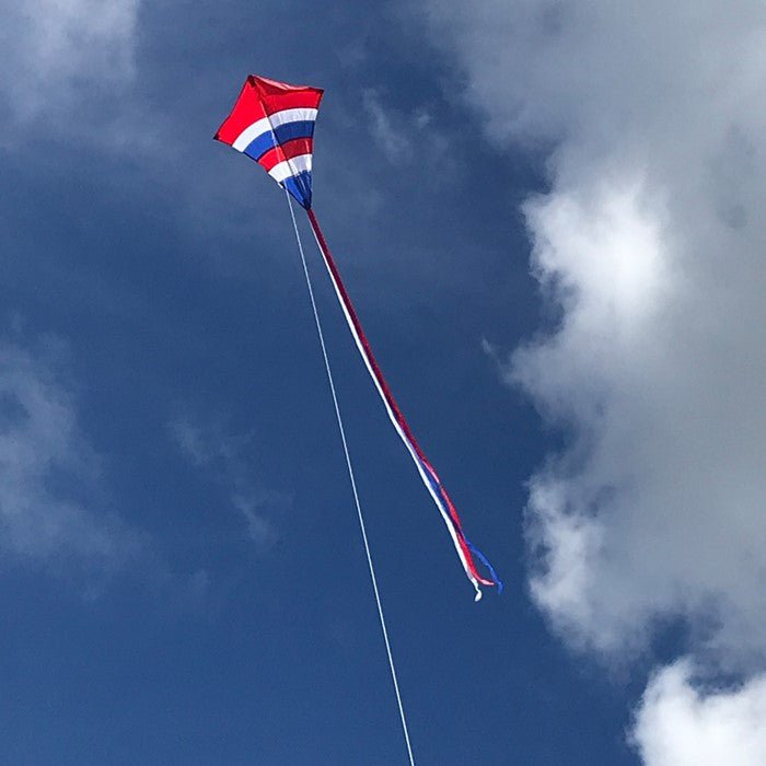 In the Breeze Patriotic Arch 27" Diamond Kite flying high in the sky with long fabric tails against a backdrop of clouds.