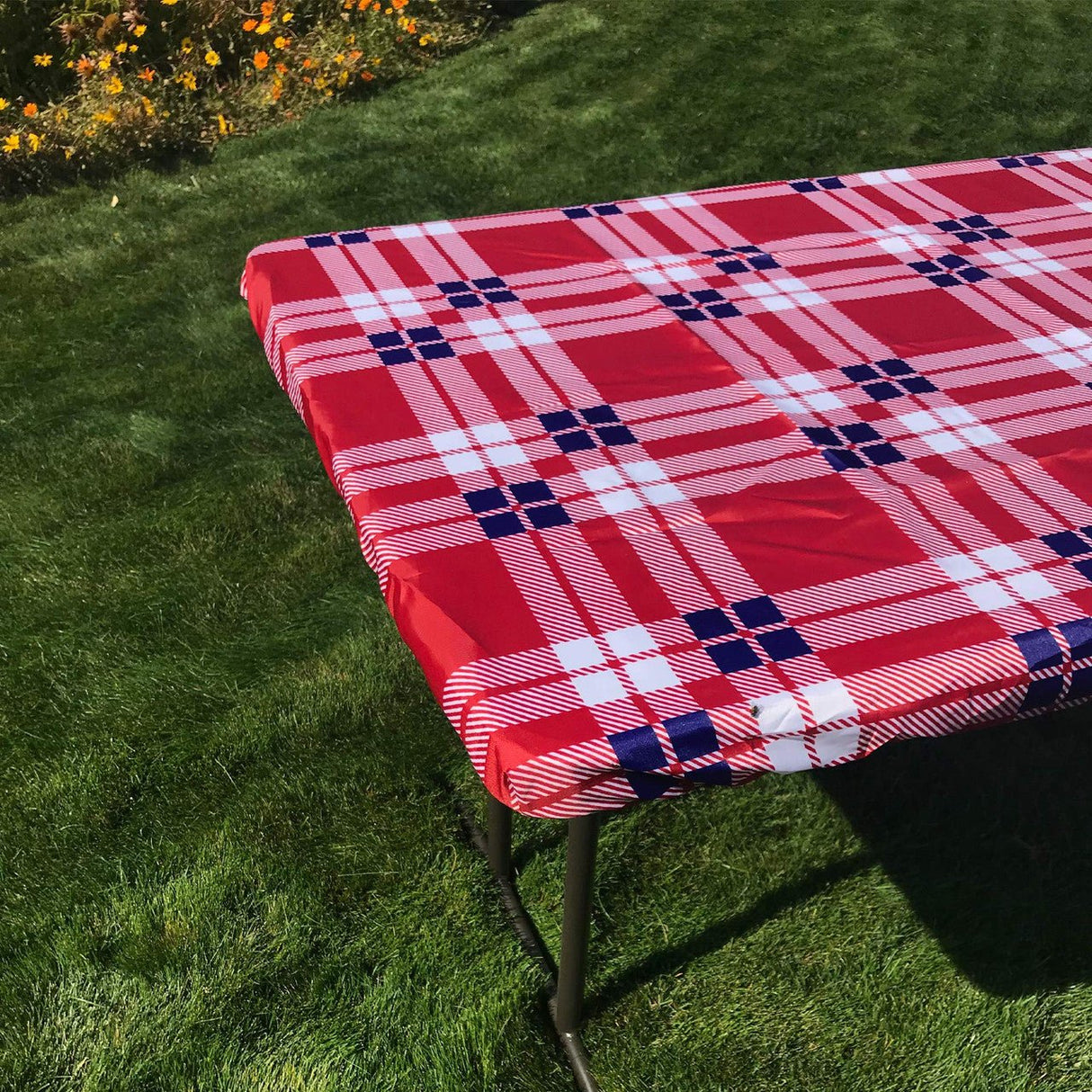 Red and white plaid fitted tablecloth on a picnic table outdoors, featuring water and stain-resistant fabric with elastic pockets.