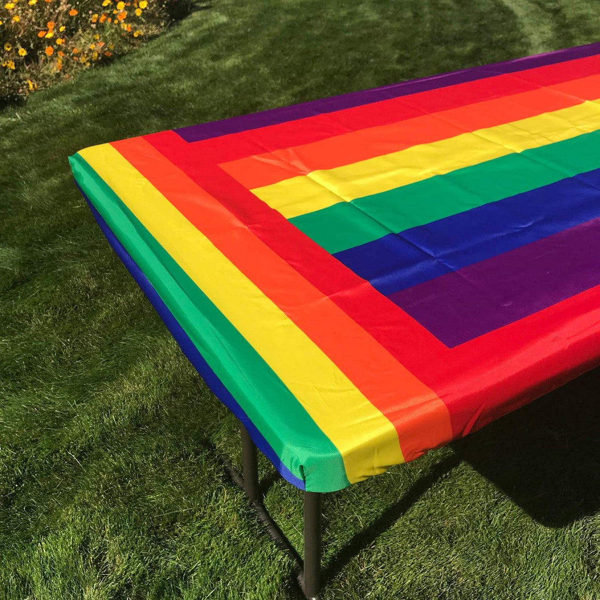 In the Breeze Rainbow 6 Foot Fitted Tablecloth on an outdoor picnic table with colorful stripes, secured with deep 4" pockets.