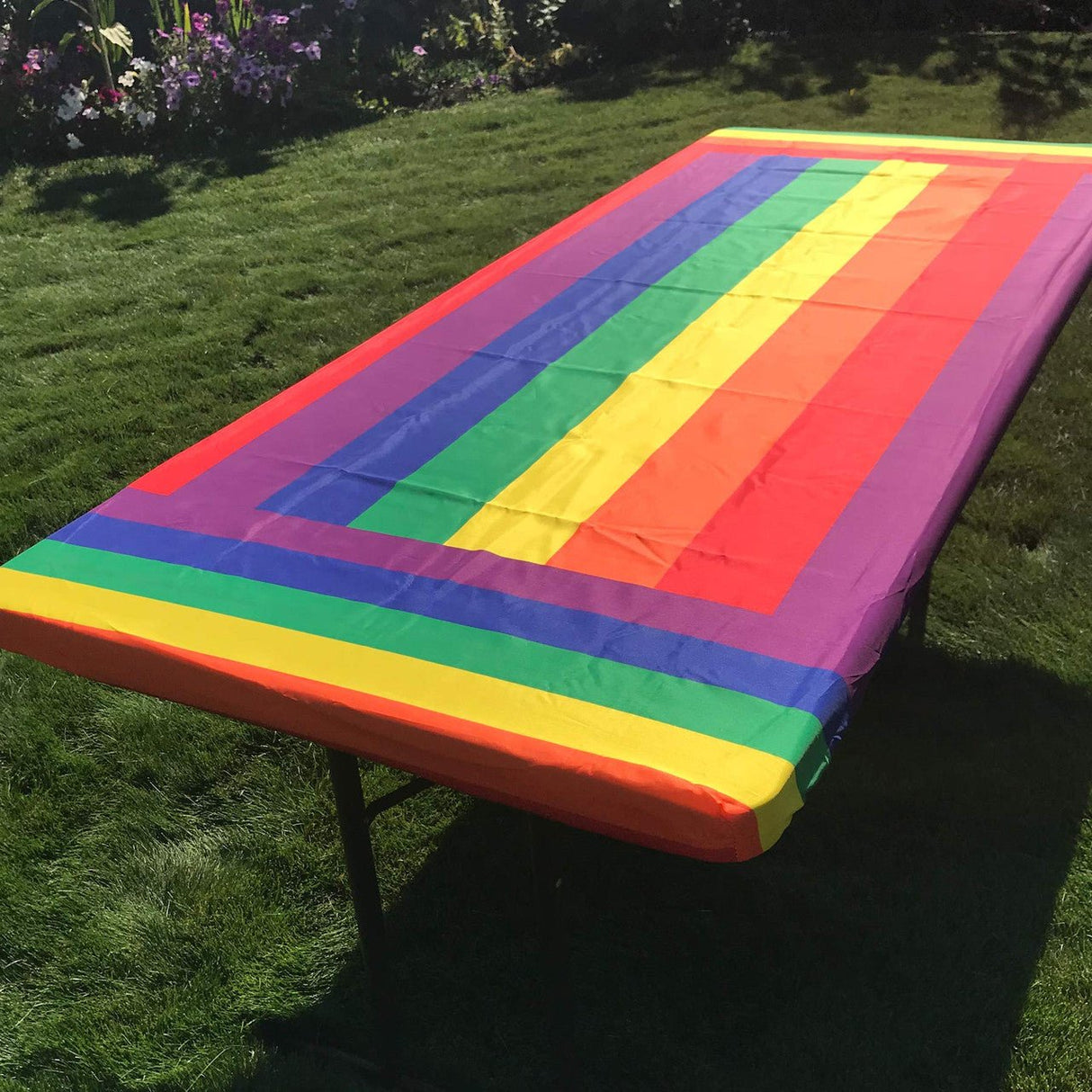 In the Breeze Rainbow fitted tablecloth on a 6-foot outdoor table with green grass background.