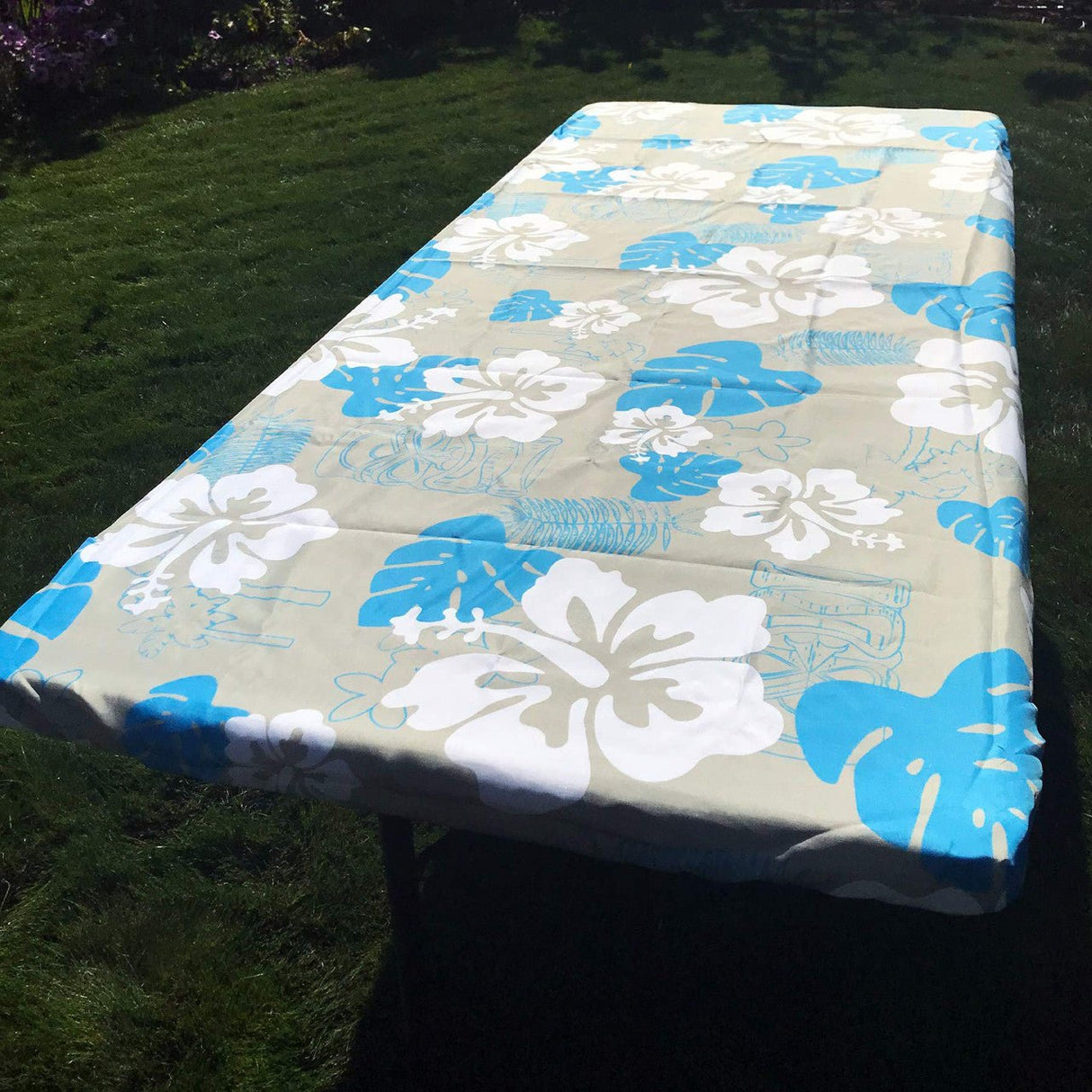 In the Breeze Tropical 6 Foot Fitted Tablecloth with blue and white floral design on a picnic table outdoors