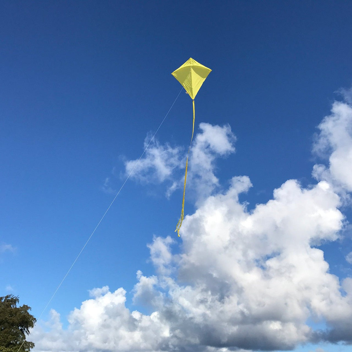 Yellow Colorfly 30-inch Diamond Kite flying against a blue sky with white clouds