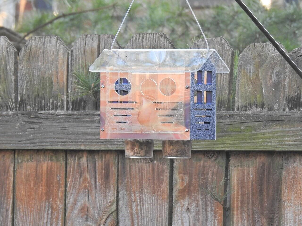 JCS Wildlife Enclosed Bluebird Feeder 2.0 hanging on a wooden fence, designed for bluebirds with multiple entrance holes.